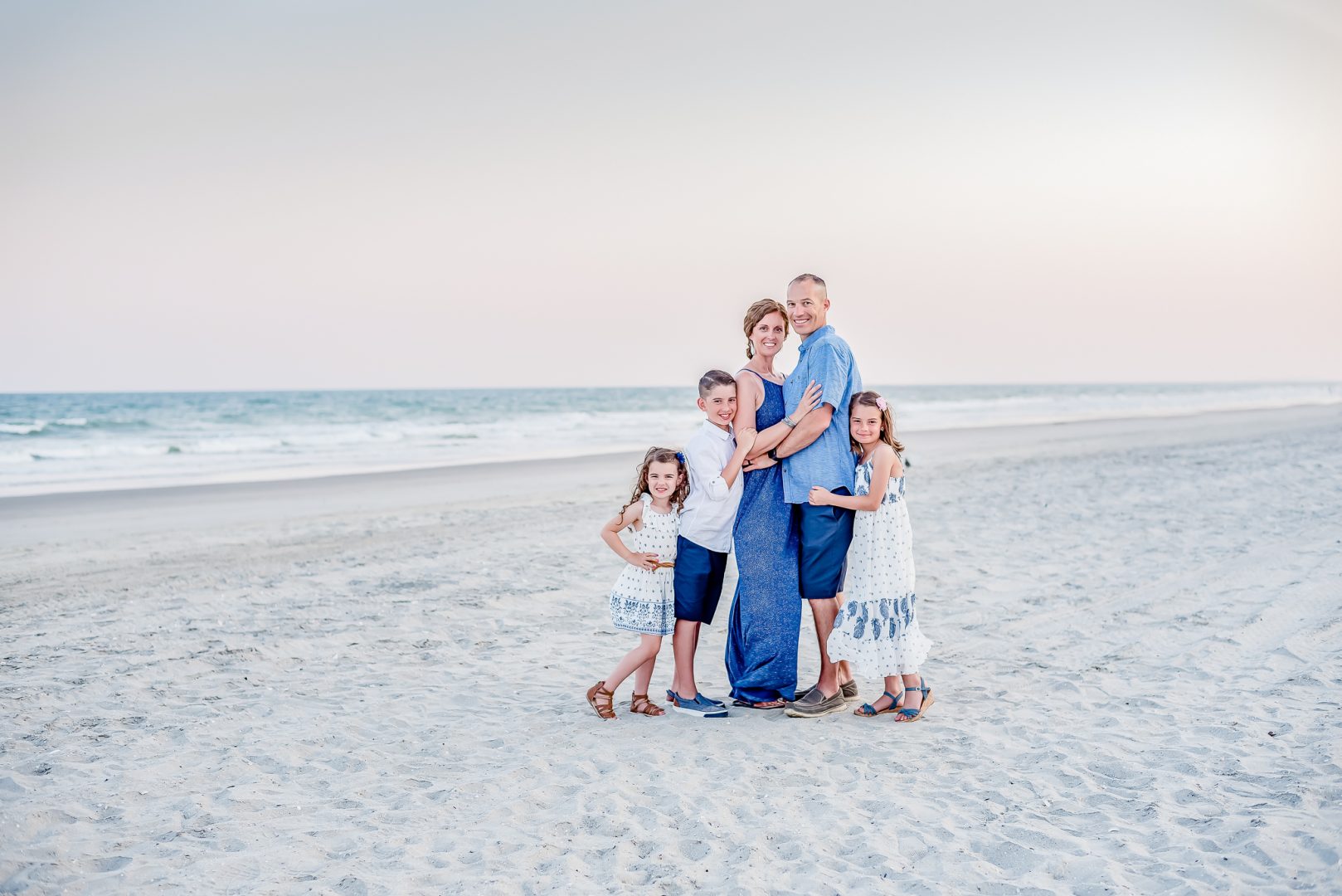 A family of five in blue and white on the beach in Wrightsville Beach, NC, at sunset.