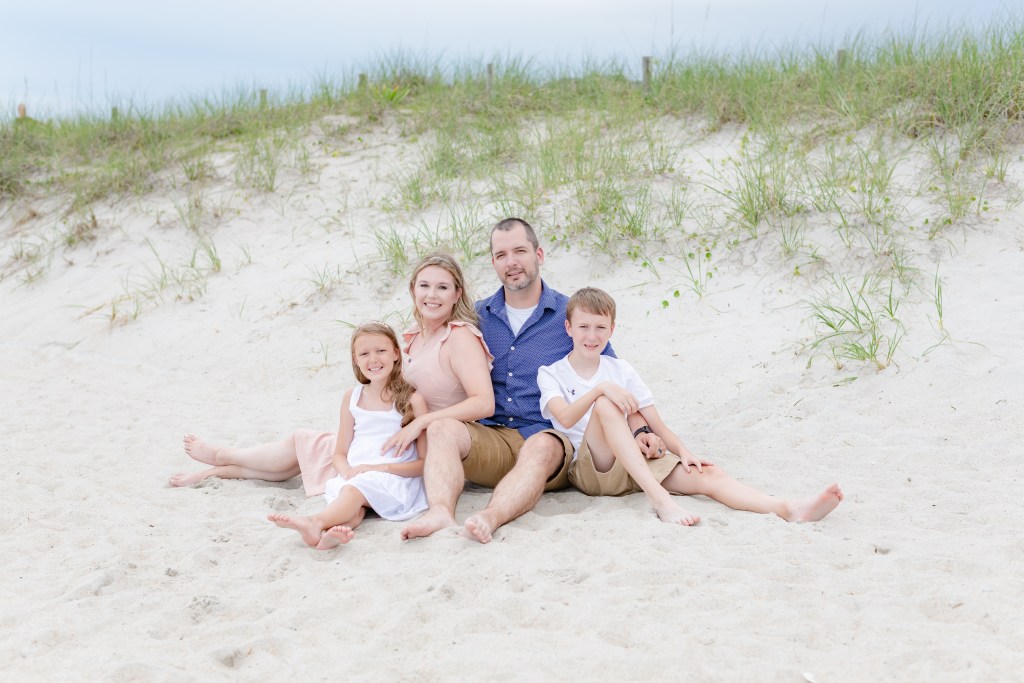 A family of four sitting in the dunes on the beach.